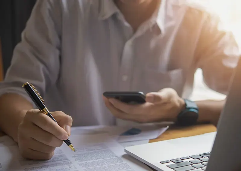 Un homme écrit au stylo avec son téléphone en main